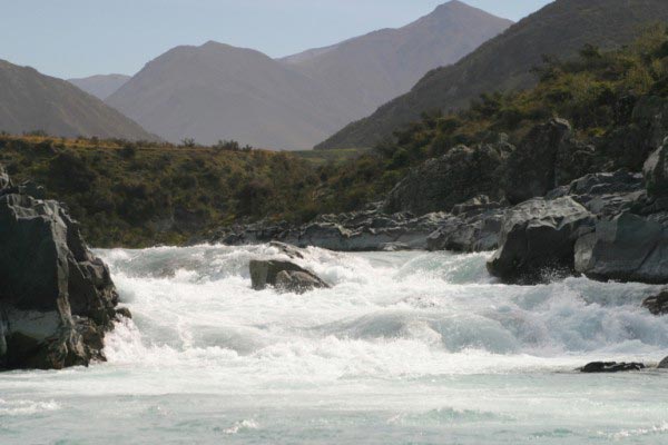 Water rages down the rapids section of this long river. The white water flows at a high speed as it forces its way through the rocks.